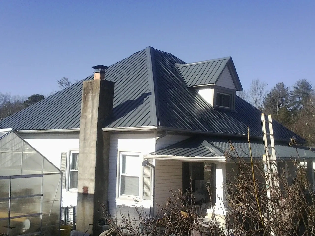 Dark blue standing seam metal roof on a white farmhouse with dormer — Slate & Tile Roof Repair by Roofing Brothers in South Fulton