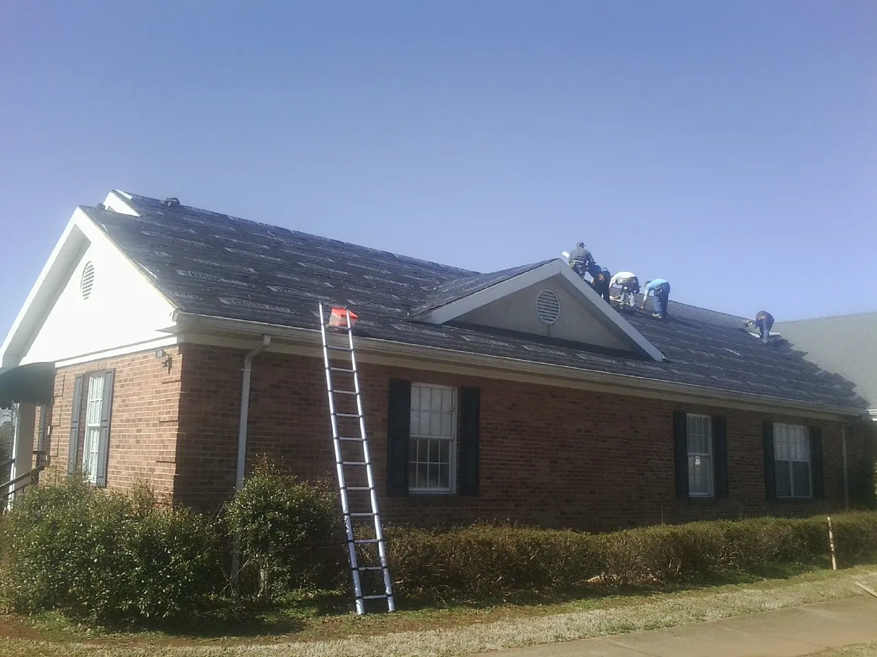 Crew tearing shingles off a brick ranch roof with a ladder set — Metal Roof Repair work by our crew in South Fulton