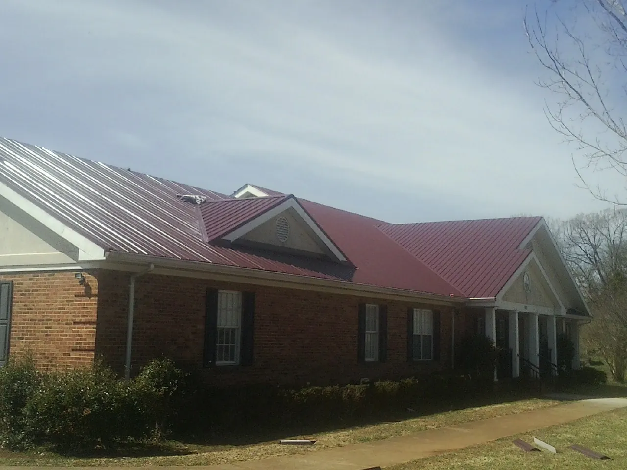 Red metal roof with gabled entries on a long brick building, from a Hail Damage Roof Repair job in South Fulton