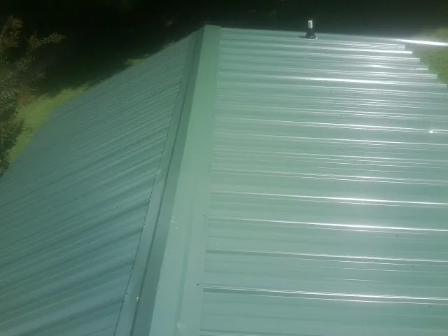 New green metal panels meeting at the ridge of a roof — Flat Roof Repair work by our crew in South Fulton