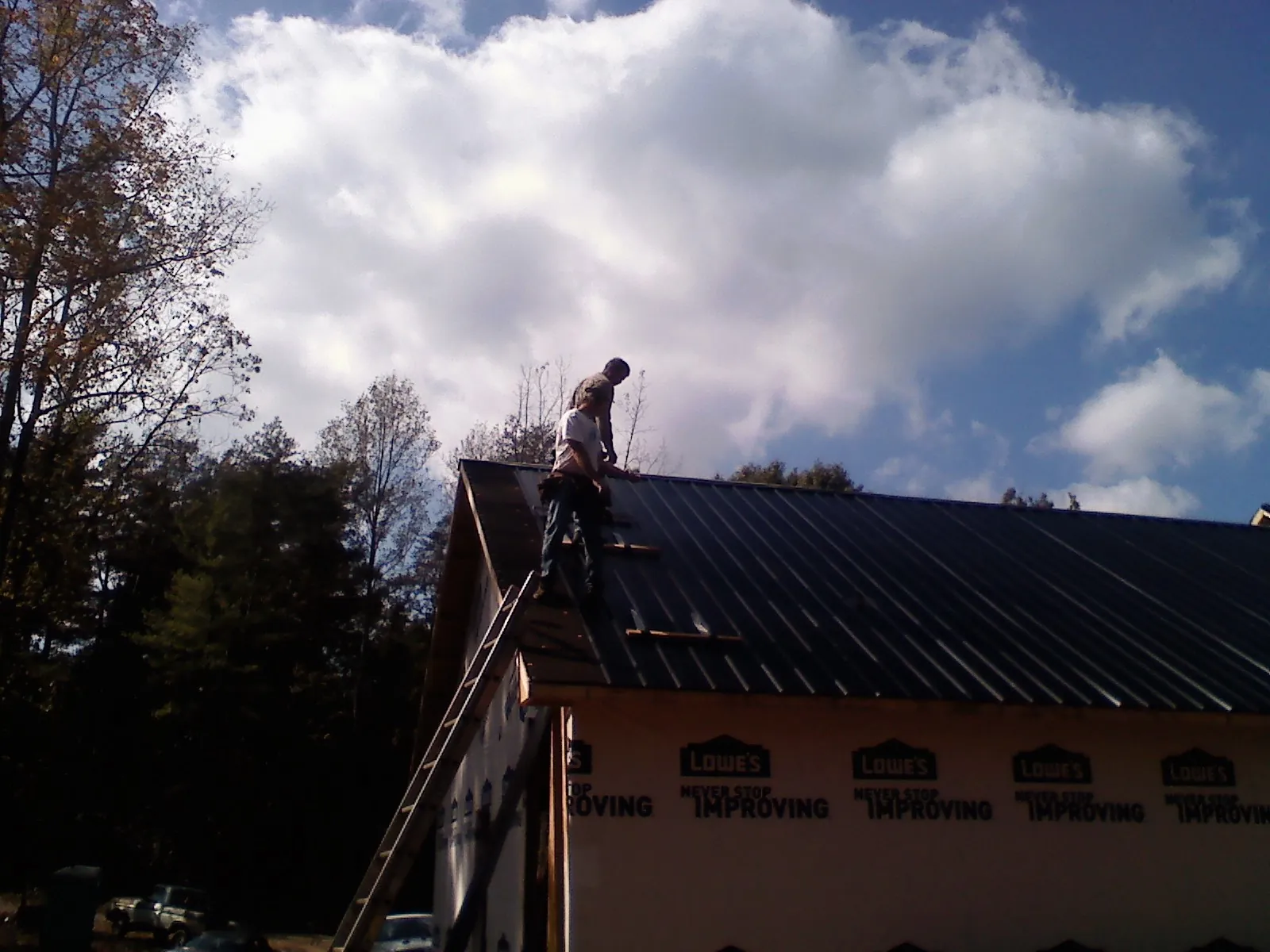 Roofer fastening dark metal panels high against a cloudy sky, from a Roof Inspection job in South Fulton