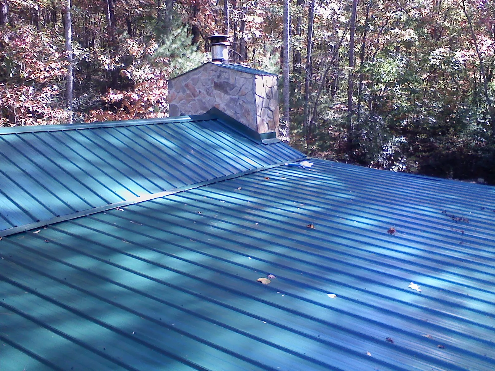 New green metal roof and stone chimney surrounded by autumn woods in South Fulton
