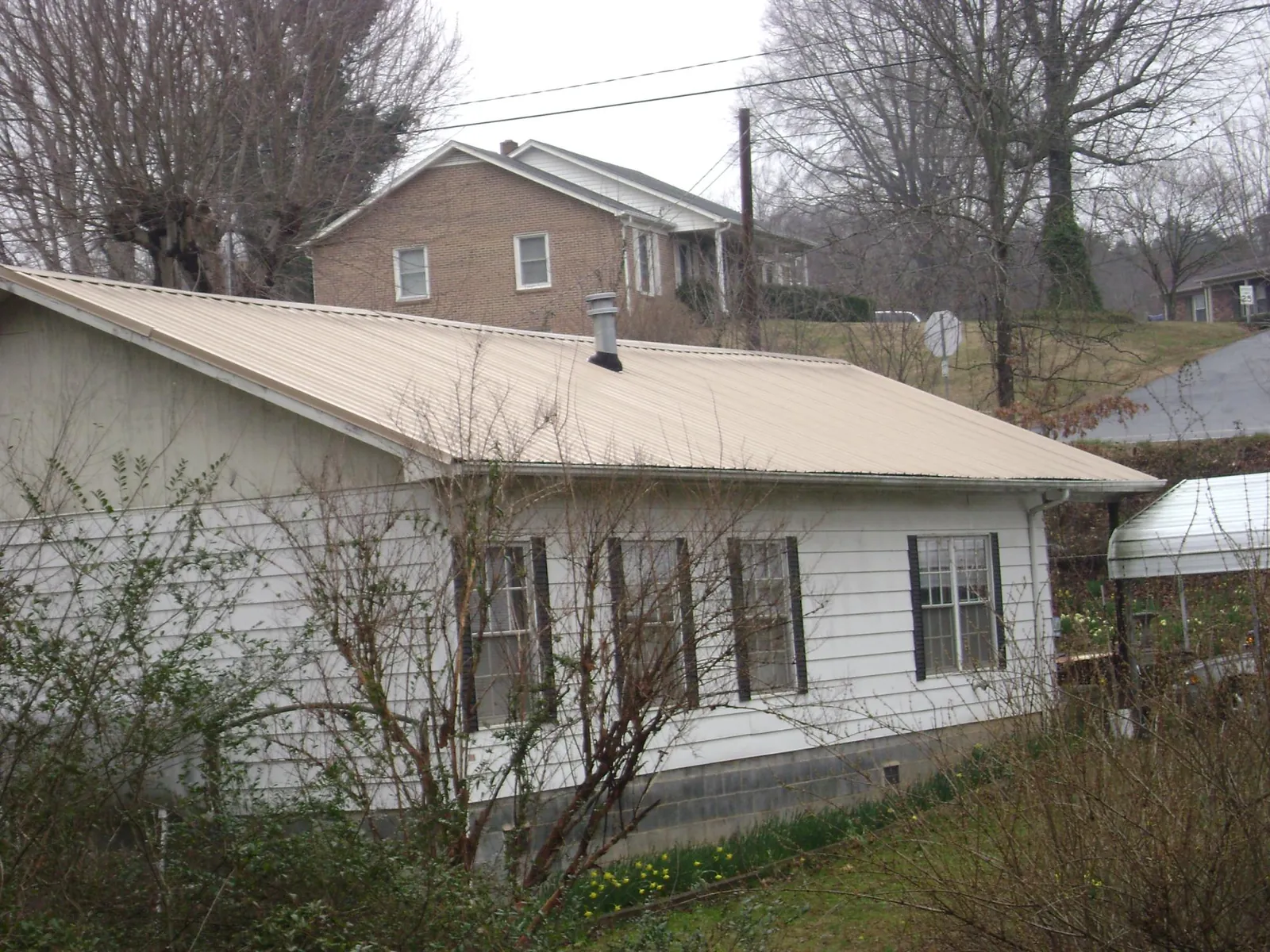 Tan metal roof on a white sided house set into a hillside — Commercial Roofing by Roofing Brothers in South Fulton